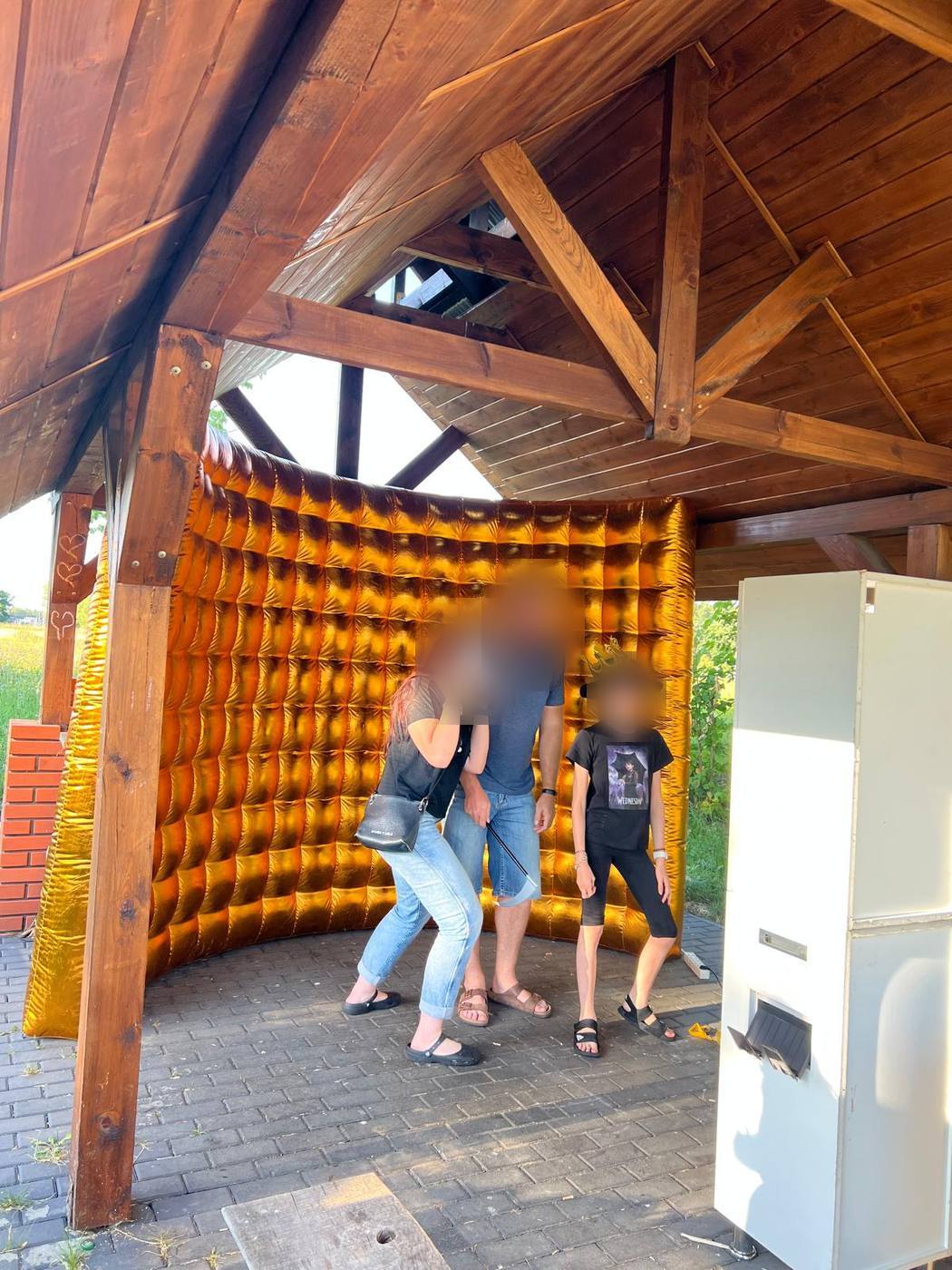 Goście w gadżetach pozują przed złotą ścianką, obok biała fotobudka klasyczna